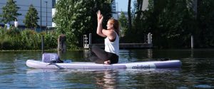 Francis op een Yoga Sup in het midden van het water. Ze stretcht haar armen.