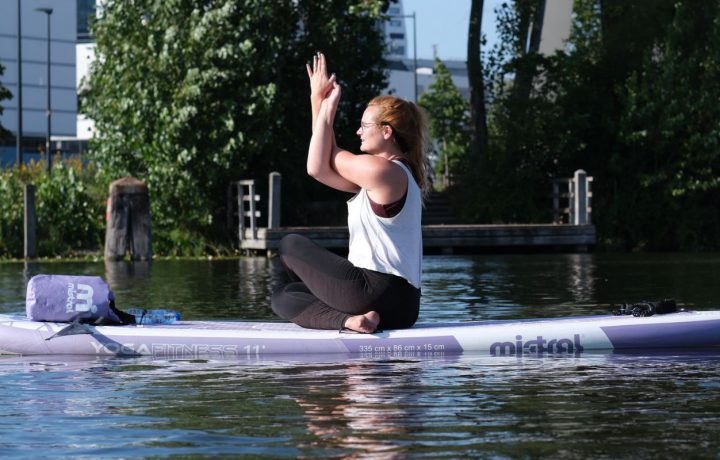 Francis op een Yoga Sup in het midden van het water. Ze stretcht haar armen.